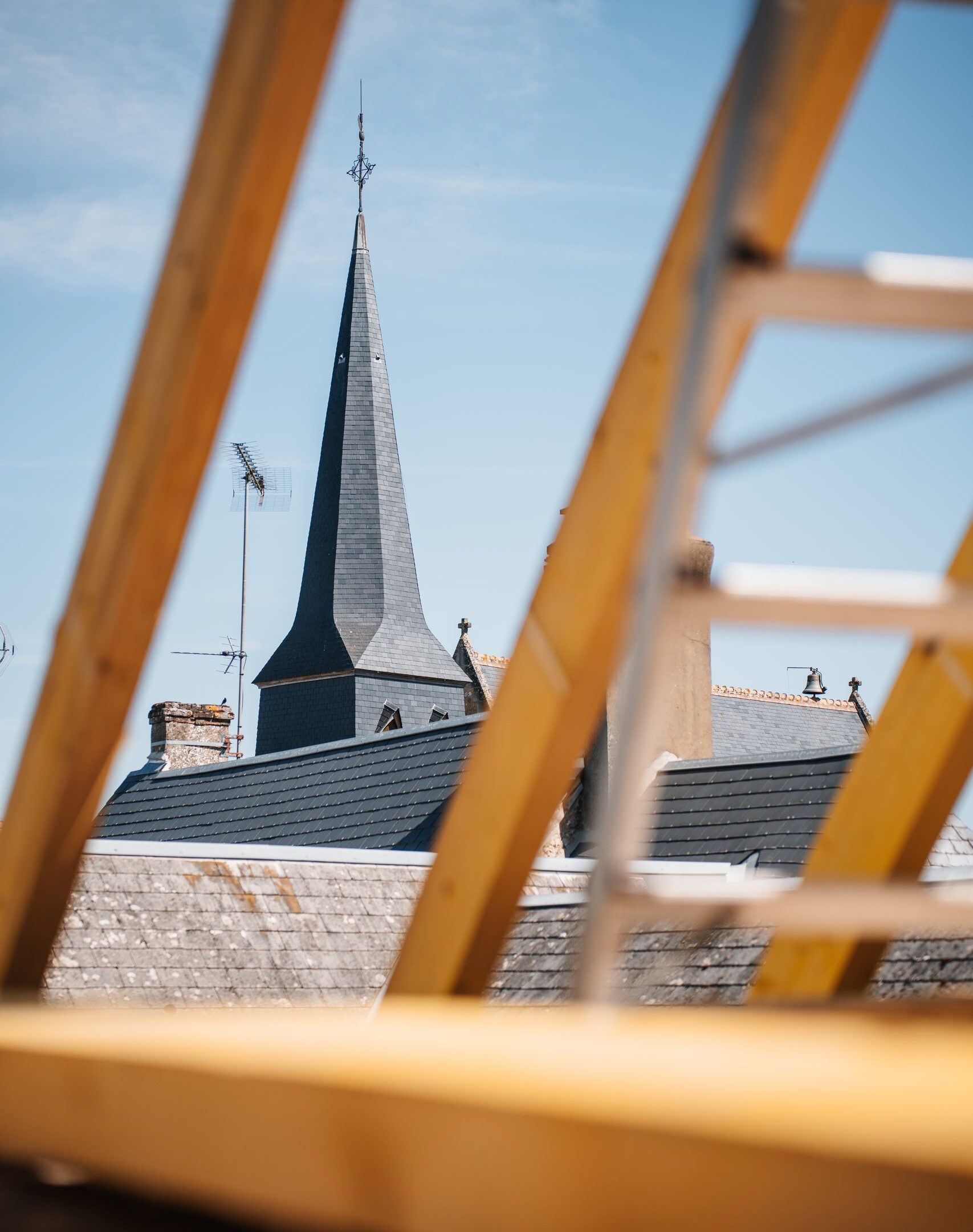 View of a church spire through the framing of a rooftop construction site under clear skies.